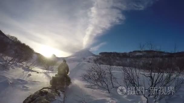 雪地摩托骑雪路上背景喷发火山视频