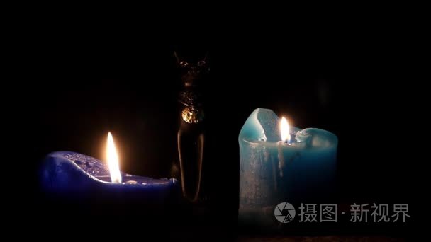 两个点亮暗蓝色的蜡烛和埃及的黑猫小雕像之间他们在晚上