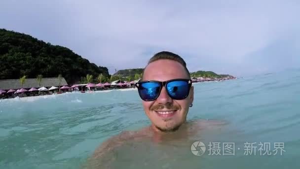 年轻英俊的白种人男人太阳镜开心和微笑热带巴厘岛，印度尼西亚的海洋里。Pandawa 海滩。慢动作