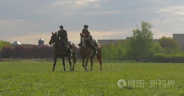 奥波莱市天两个骑兵，老式统一士兵在草地上的人在阳光明媚的春天天游行正在背景城市景观公园里走