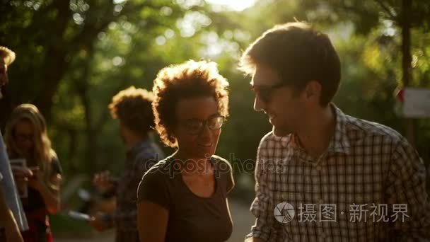 非洲裔美国女性笑笑跟白人男性太阳镜和表在公园里和朋友一起在慢动作中背景上