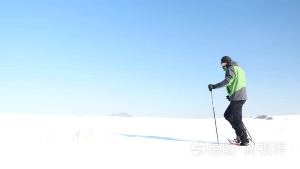 冬季旅游与雪鞋走在白雪皑皑的漂移。绿色运动夹克和黑色徒步裤子粉雪的雪鞋的徒步旅行者。多云的冬季一天，温柔的风带来小雪花