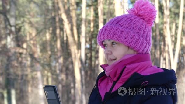 在冬季森林制作照片从移动的女人，她是在粉色的帽子和外套，外面阳光明媚的一天