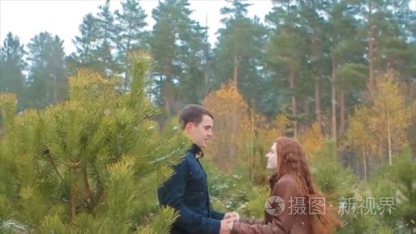 年轻夫妇手牵着手跳在秋天森林在雪中