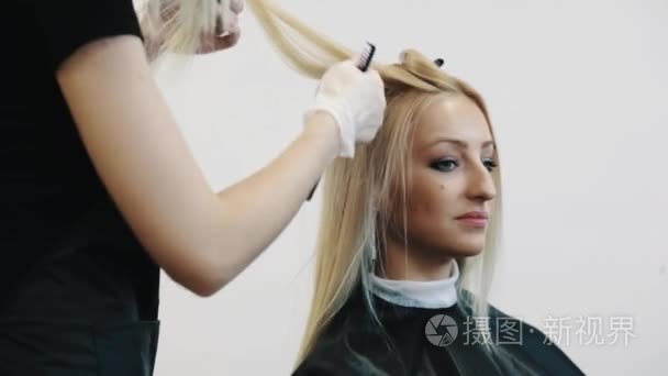 理发师在手套使用梳子, 发夹上染成金黄色的头发,在美容店短视频