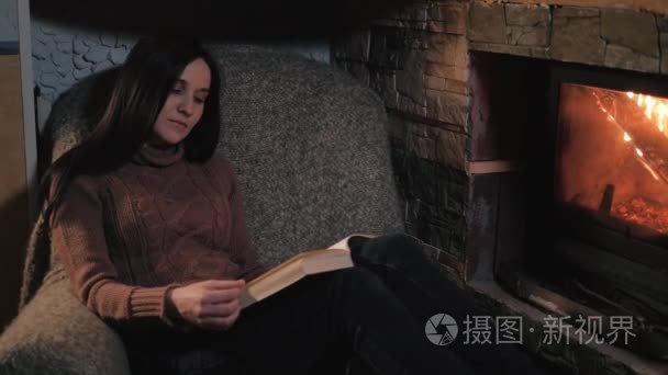 美丽的年轻女子，读本书坐在壁炉的乡间别墅。关闭了铅球 假日 生活方式的概念