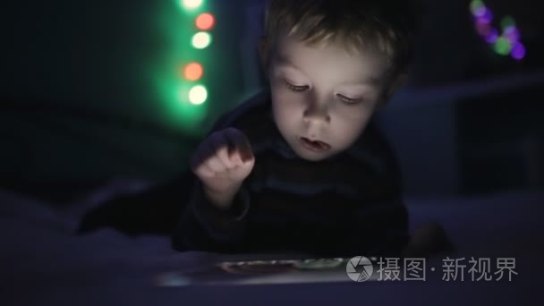 在晚上玩平板电脑或智能手机在床上的小男孩