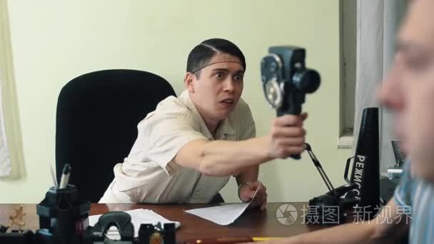 净的头发的男人使用复古 8 毫米摄像机在办公室位访客