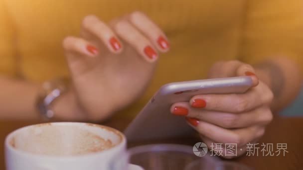 女人坐在咖啡桌旁，在她的手机上打字与她薄修剪的手指