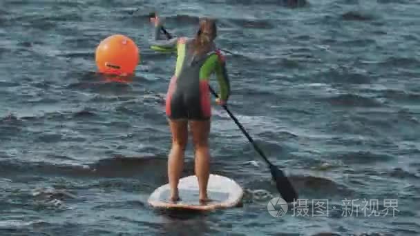 俄罗斯圣彼得堡-2016 年 8 月 28 日︰ 远射的妇女在充分泳衣摇摇欲坠试图骑用的球拍冲浪板