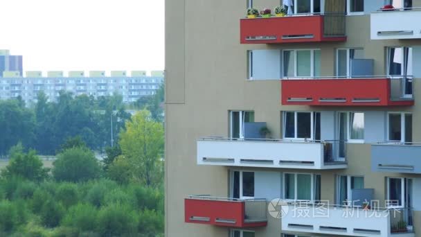 在城市地区，树，更多的建筑物和明亮的天空背景下的一栋公寓楼的多彩阳台