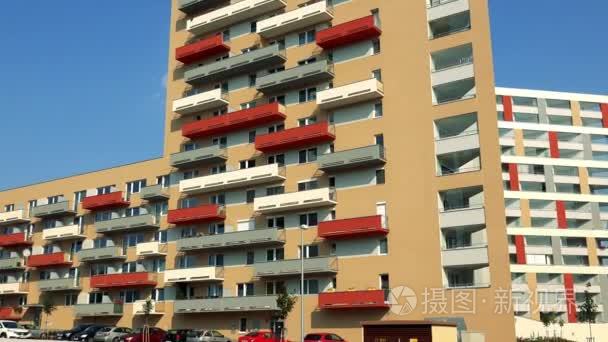 在城市地区、 下面的停车场、 蓝蓝的天空和另一个公寓建设中的背景，在前景草丰富多彩 （红色、 灰色、 黄色） 阳台米色公寓楼
