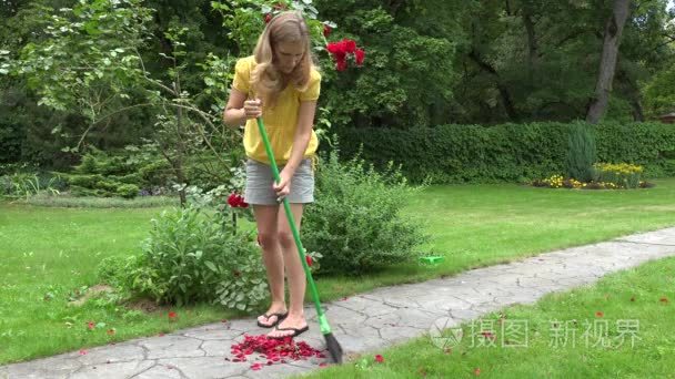 与女人扫扫把在花园小径上的玫瑰花瓣。4 k