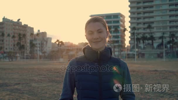 美丽迷人的年轻女子站在沙滩上，微笑对着摄像机。日落海棕榈度假村酒店视频