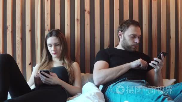 夫妻坐在床上，不互相交谈，在智能手机上打字。年轻的男人和女人有争吵视频