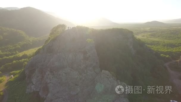 人们挥舞着相机飞过小山上。一个人想要把石头扔进一架无人驾驶飞机