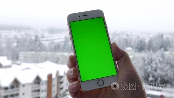 男人握与您自己的自定义内容和雪自然背景的绿色屏幕空白智能手机