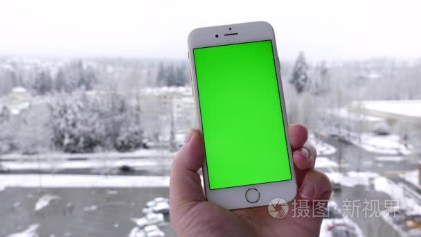 男人拥有空白智能手机和攻丝与雪自然背景的绿色屏幕上