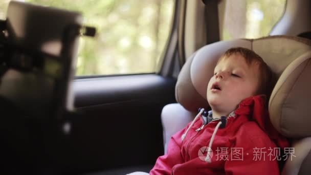 可爱的小男孩与张着嘴坐在窗户旁边车椅子。累了的孩子在车里