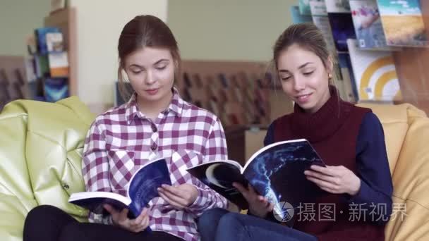 两个友好的女学生在阅览室翻阅杂志