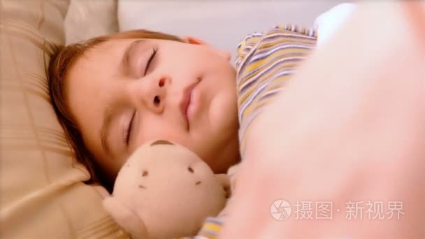 3 岁的小男孩睡在一起的泰迪熊的画像。他母亲的手抚摸他