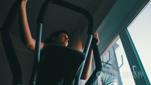 剪影的女孩行使对有氧运动教练交叉训练机在家上的窗户