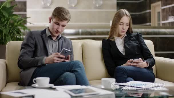 年轻的女人和男人坐和使用他们的智能手机