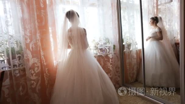 美丽的新娘在典雅婚纱走到窗口前的婚礼。后视图