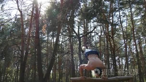 强大的肌肉男做倒立在森林里。肌肉发达的男性健身家伙做日志在木头上的特技。运动员训练执行倒立在外肌。健身运动健康的生活方式