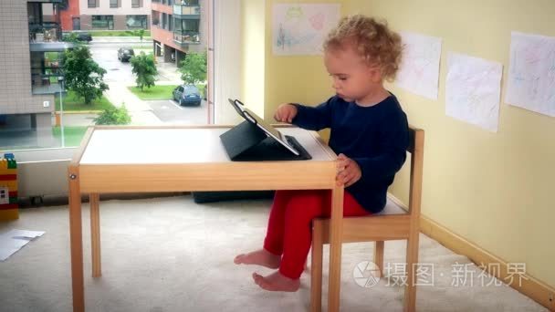 可爱的孩子玩平板电脑坐在桌子旁边的小椅子上
