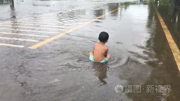路上，道路被淹，快乐的亚洲男孩玩水后重雨在晚上