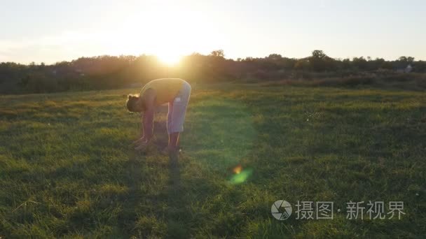 练瑜伽的年轻人移动和定位在草地上的绿草。运动型的家伙站在自然的瑜伽姿势。作为背景的美丽景观。健康积极的生活方式的瑜伽户外