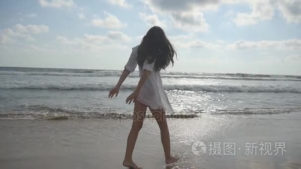 幸福的女人走路和纺纱海洋附近的海滩上。年轻漂亮的女孩享受生活，在海边玩。暑假或假期。在背景的自然景观。慢动作