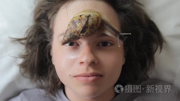 一个年轻人在水疗中心接收与非洲漱口褐云的面部按摩。蜗牛吃死皮制作的。最后，它使皮肤光滑和新鲜
