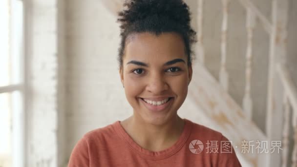 美丽的非洲裔美国女孩笑着，看着相机的特写肖像。女人从严重的脸上笑在家情绪的表达