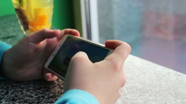 十几岁的年轻旁肉桂柠檬奶茶咖啡厅里的智能手机上玩游戏