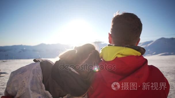 白种的女性和男性头山滑雪场在他肩膀上坐着。与太阳耀斑在慢动作的背影