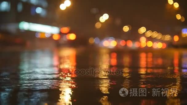 多彩的交通灯景圈反映在夜间城市街道与小雨滴的水中。慢动作视频