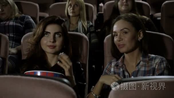 电影院里。三个漂亮的女性朋友看一部电影，在电影院里吃爆米花。高清