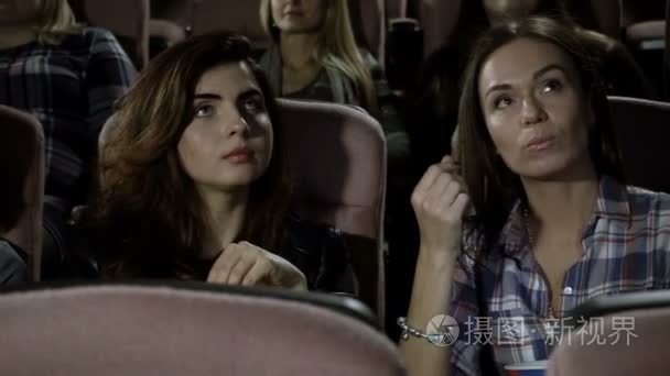 电影院里。三个漂亮的女性朋友看一部电影，在电影院里吃爆米花。高清