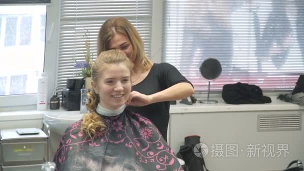 一个年轻女子在一家美容院的肖像 从卷发创建一个壮观的设置。一位金发女郎在一名理发师做漂亮的发型啊。头发护理和创建映像视频