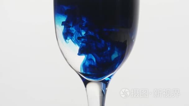 蓝色的墨水滴入一杯水在白色背景上玻璃概念中的毒药