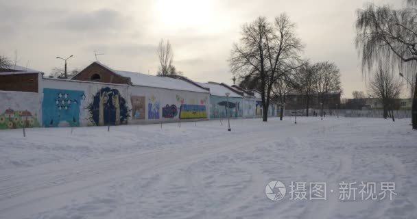 白雪皑皑的地面和废弃建筑物车库画涂鸦冬季步行由 Konotop 小省市雪的城市边缘地面光秃的树木