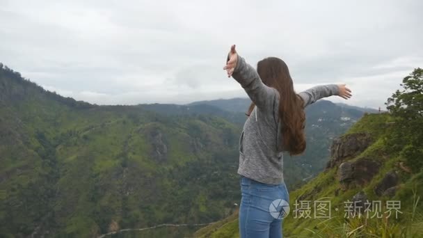 女游客站在美丽的峡谷的边缘，凯旋扩张军备了。年轻女性的徒步旅行者到达顶山和举的手上。慢动作