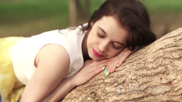 美丽的女孩在公园里躺在树枝上的梦想。美丽的黑发微笑和大笑。慢动作