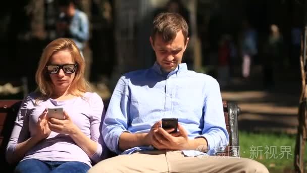男人和女人在不同的方向，坐在板凳上看。大家都看他的手机
