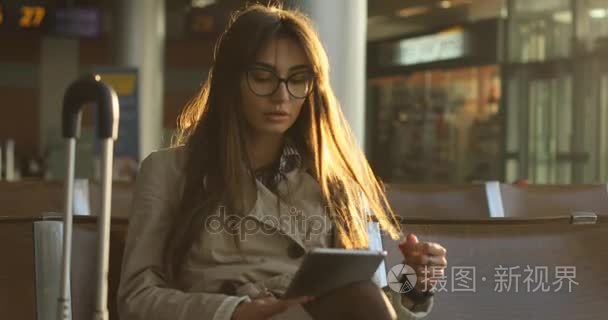 漂亮的年轻女乘客浏览平板电脑与背包和国际机场，检查她的智能手表在手提行李携带