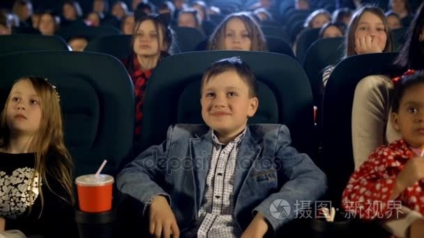 小女孩和小男孩看一部电影，电影院里吃着爆米花