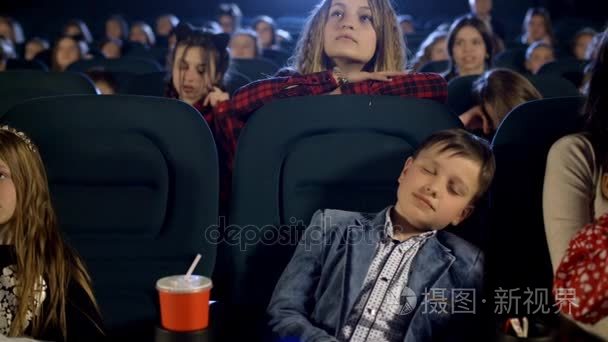 昏昏欲睡的男孩害怕在电影院。孩子们看着大屏幕上的卡通