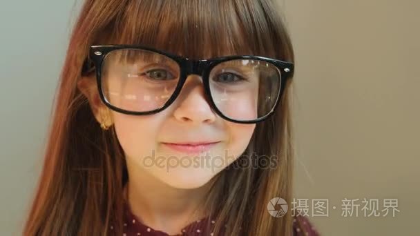 有趣的小女孩，穿上成人的大眼镜。在相机上开心的小女孩。关闭。灰色背景